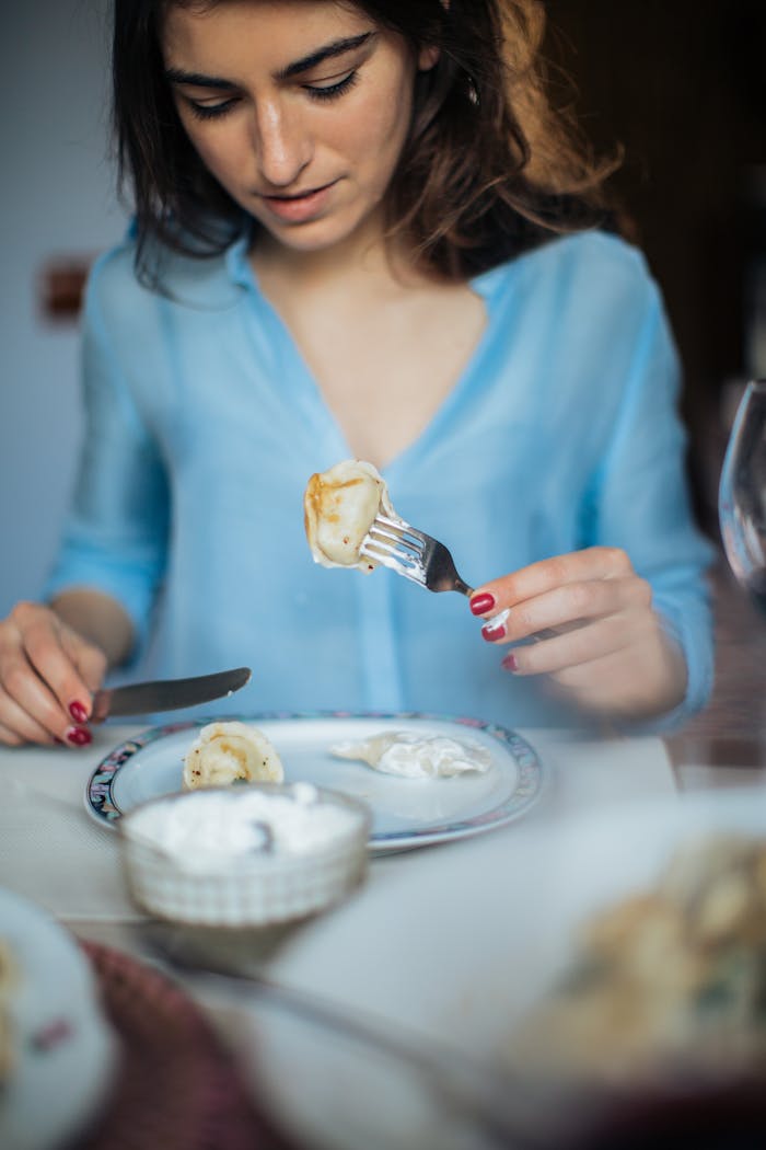 services-02 Young woman savoring traditional Russian pelmeni dumplings with sour cream in a cozy indoor setting.