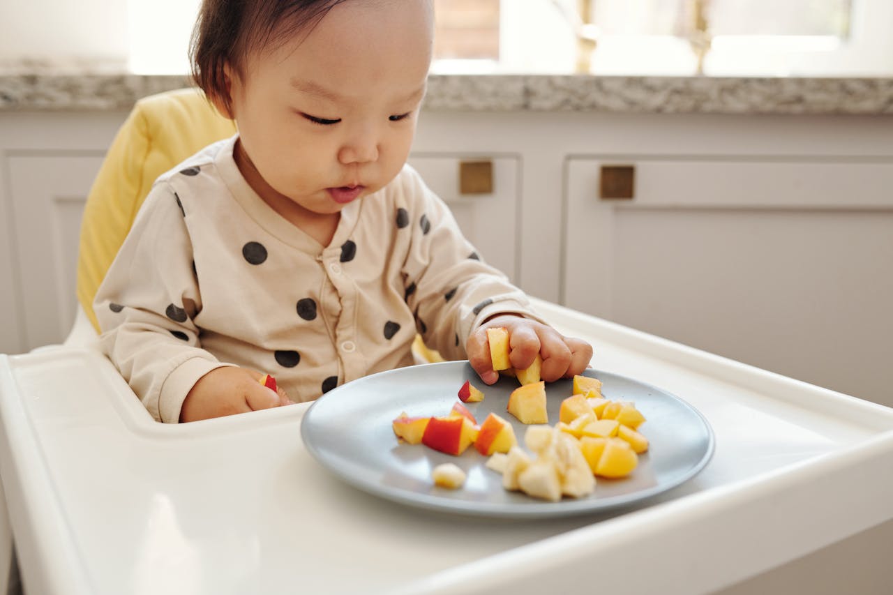 about-us-01 Adorable baby enjoying fresh fruit slices in a modern kitchen setting.