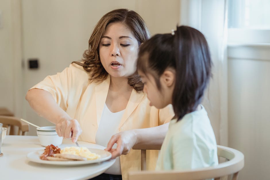 A loving mom feeds her daughter breakfast in a cozy kitchen setting.